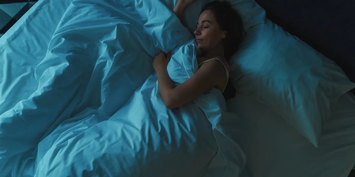young beautiful girl or woman sleeping alone in big bed at night, top view, blue toned