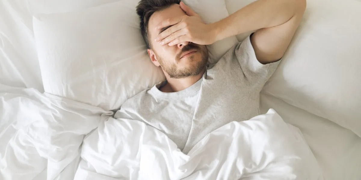 tired young man in bed closing his eyes before waking up hangover morning sleep disorder and problems