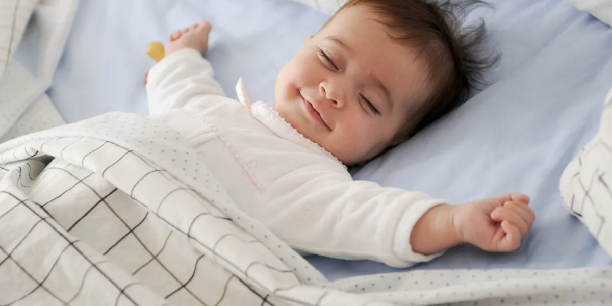 smiling baby girl lying on a bed sleeping and smiling on blue sheets