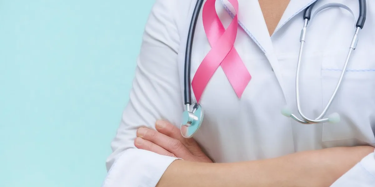 doctor with folded arms and a stethoscope on his neck, shows a pink ribbon close-up on uniform on a blue background