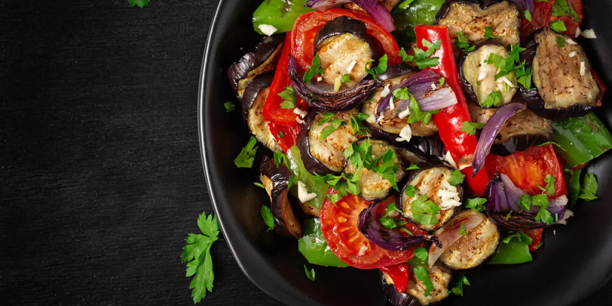 grilled vegetables eggplant, bell pepper, zucchini, red onion, tomato with garlic on a black plate top view, above
