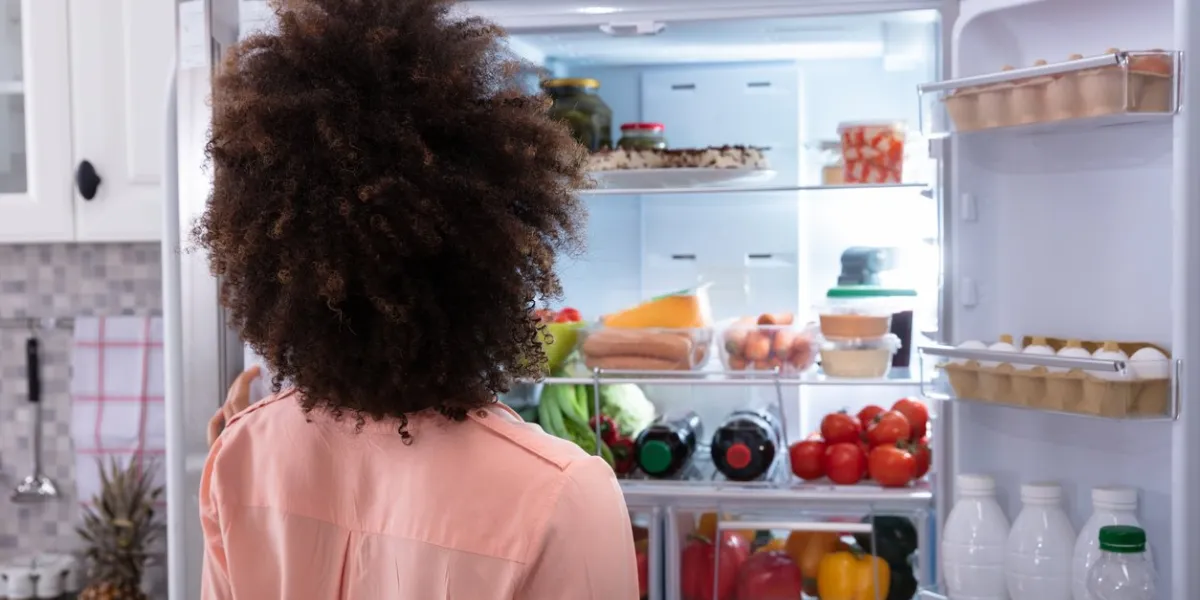 rear view of a confused woman searching for food in an open refrigerator