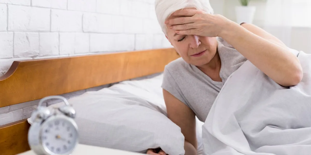 upset senior woman suffering from headache in bed, waking early in morning, touching her forehead, panorama with empty space
