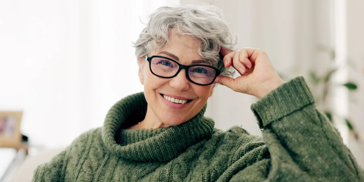 happy, face and senior woman on sofa to relax in home or grandma laughing with happiness and freedom in retirement portrait, elderly person and smile in living room, house or thinking of good memory