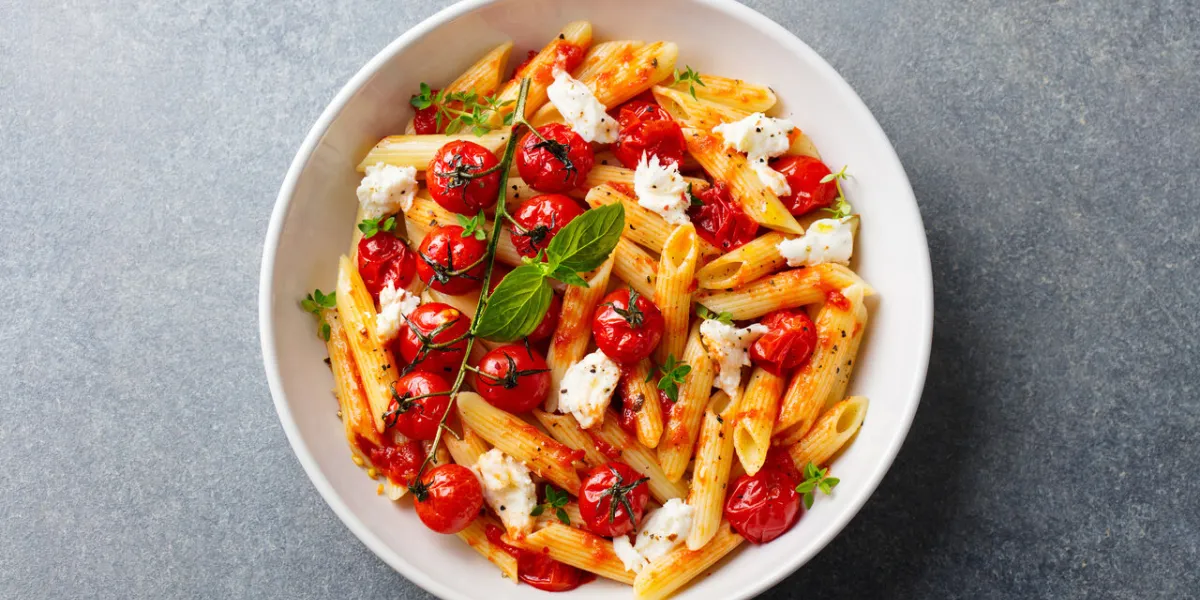 pasta penne with roasted tomato, sauce, mozzarella cheese grey stone background top view