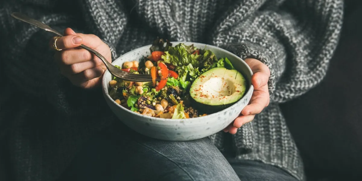 healthy vegetarian dinner woman in grey jeans and sweater eating fresh salad, avocado half, grains, beans, roasted vegetables from buddha bowl superfood, clean eating, dieting food concept