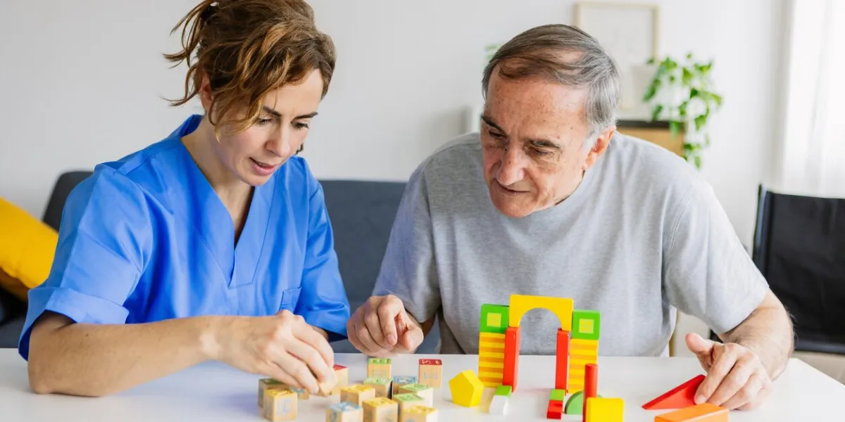 female caregiver and senior man playing wooden shape puzzles game for dementia prevention
