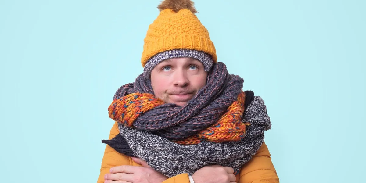 handsome caucasian funny man in several hats and scarfs looking up being confused on blue background winter fashion