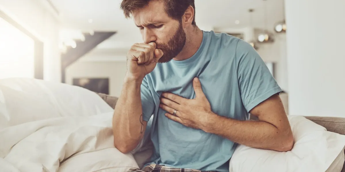 sick, coughing and man on a sofa with chest pain problem, tuberculosis or influenza at home asthma, anxiety and male person with breathing trouble in living room with covid, pneumonia or lung virus