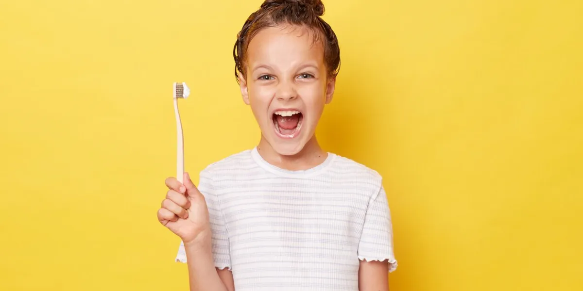 excited little girl with wet hair wearing casual white t-shirt standing isolated over yellow background screaming loud showing new toothbrush