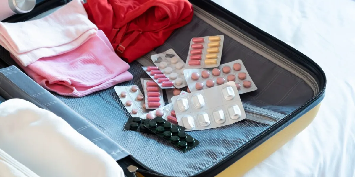 travel concept opened packed suitcase on bed in hotel room, pills and medicine