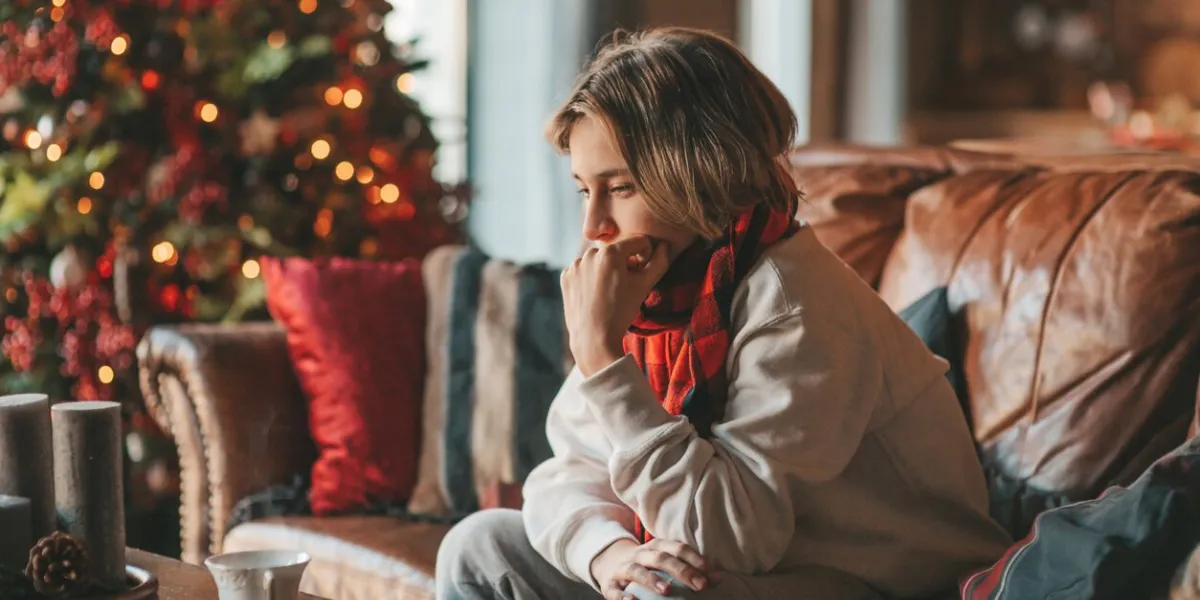 young teen boy with long hair thoughtful look sad eyes negative mood angry and crying at home stylish zoomer gen z pensive on new year holidays with xmas tree bokeh lights garlands eve 25 december