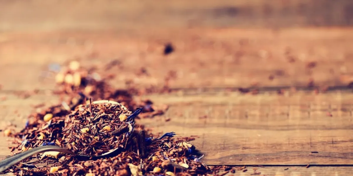 gros plan d'une cuillère avec rooibos mélangé avec des fleurs, des fruits secs et des herbes, pour préparer un thé rooibos, sur une table en bois rustique