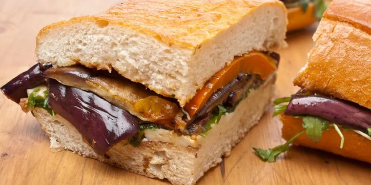 morceaux d'aubergine et poivre grillés pressés, fromage et roquette ciabatta pain sandwich sur une table en bois